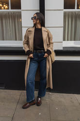 a lady in a black sweater, a long trench coat and a pair of blue jeans